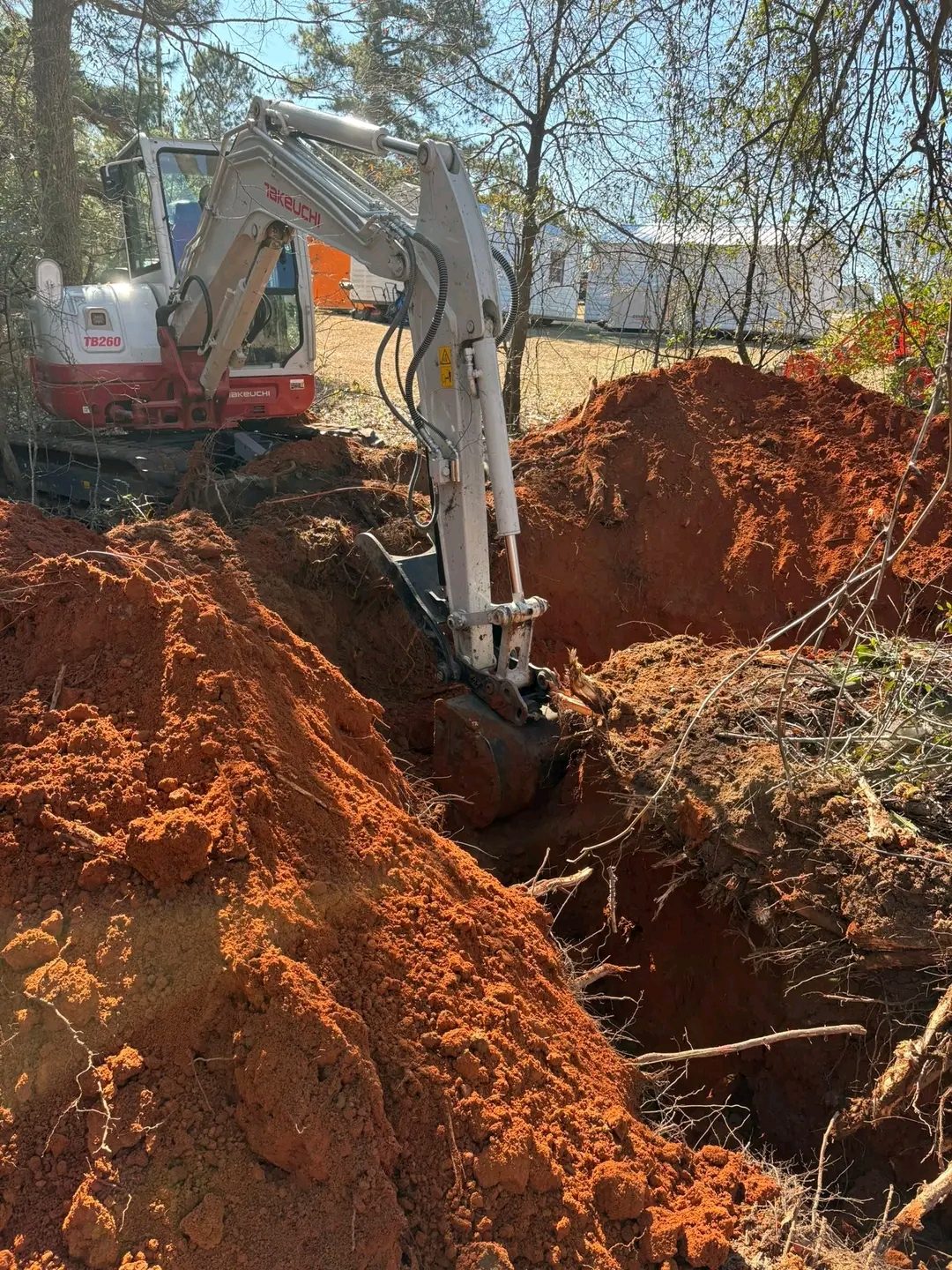 TCB Farms & Clearing excavation project — mini excavator digging a trench in red clay soil