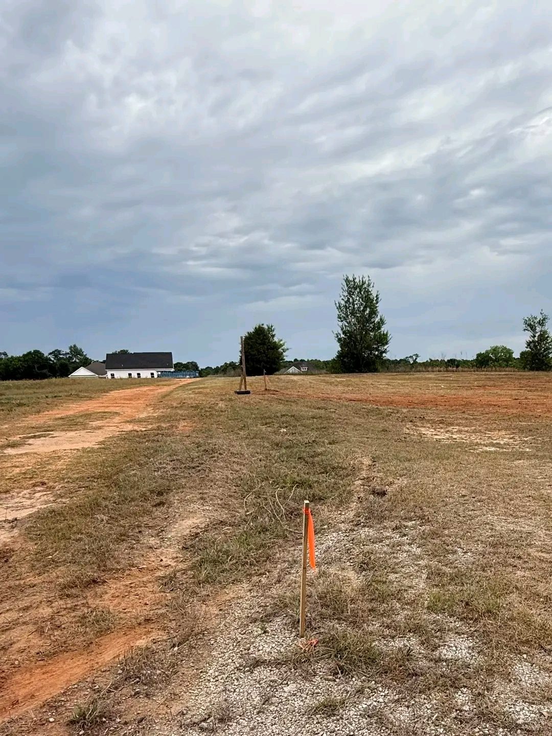 TCB Farms & Clearing grading project — survey stakes along a graded dirt path leading to a house